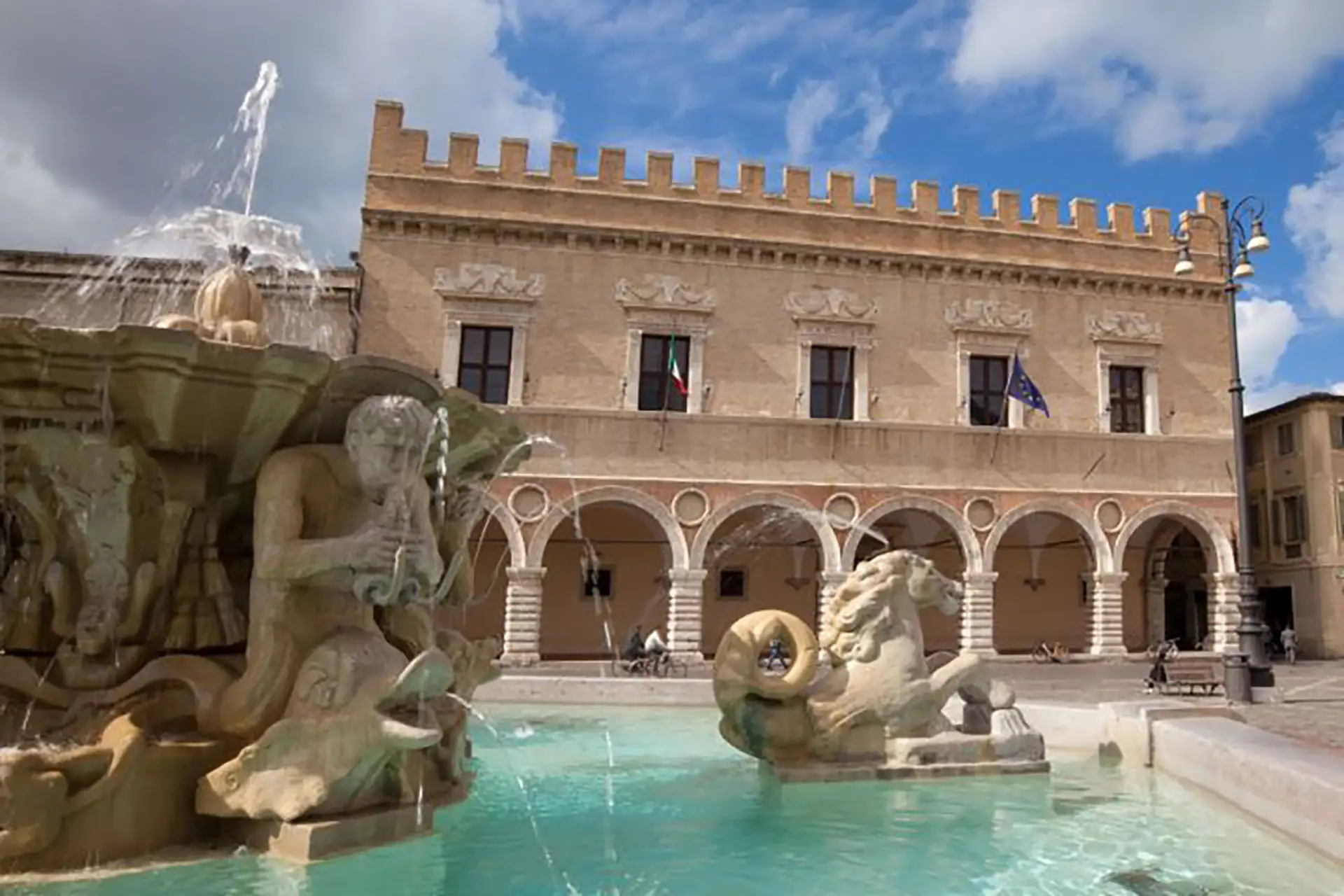Piazza del Popolo in Pesaro, Italy, featuring the baroque La Pupilla di Pesaro fountain (reconstructed in 1960) with seahorses, Tritons, and shells carved in Istrian stone and Veronese marble.