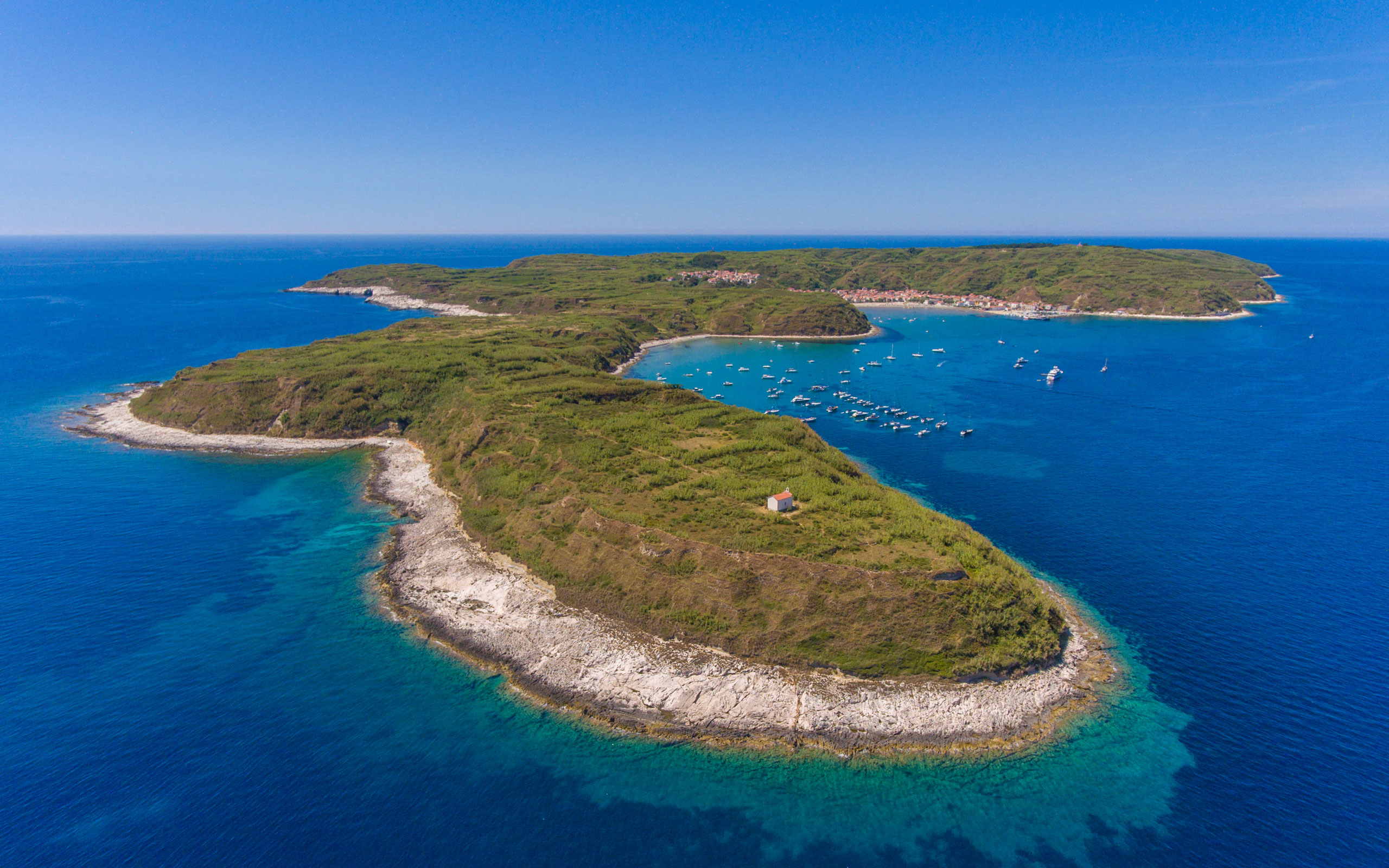 The island of Susak, the key turning point of the La Duecento regatta, showing its distinctive sandy cliffs and shallow waters.